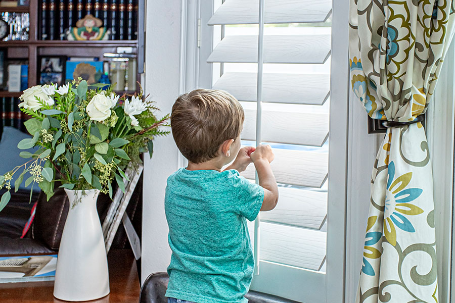 A little boy peaking through white polywood shutters