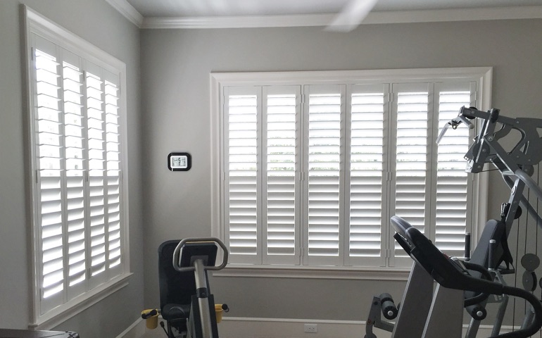 Draft-blocking window coverings are vital in rooms with windows on more than one wall. Raleigh home gym with shuttered windows.