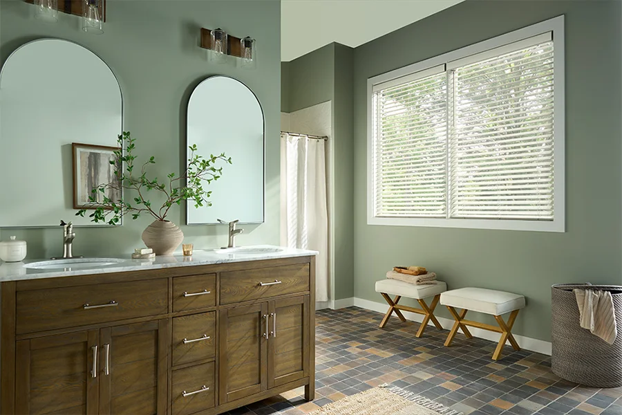 White faux-wood window blinds blend with any color scheme and hold up beautifully in moisture-rich environments. White faux-wood blinds cover a large bathroom window